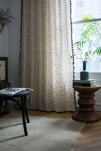 Detail of beige cotton linen curtain with gold star patterns and black fringe tassels