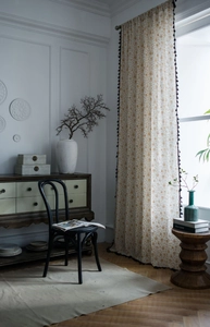 Detail of floral kitchen curtain with yellow patterns and black pom-pom trim in a room