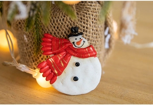 Close-up of cute snowman Christmas magnet on burlap with warm holiday fairy lights