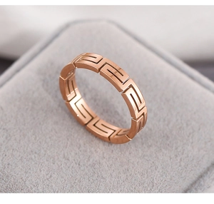 Macro detail of rose gold titanium steel ring with hollow Greek key pattern on grey velvet