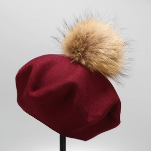 Detail of burgundy knitted wool beret with soft fluffy faux fur pom-pom on top