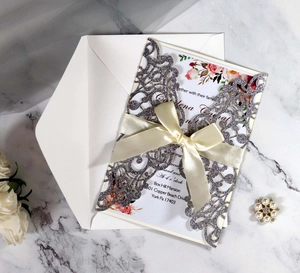 Detailed laser-cut silver glitter wedding invitation with silk bow and floral insert
