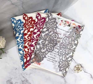 Laser-cut glitter wedding invitations in assorted colors on a marble surface