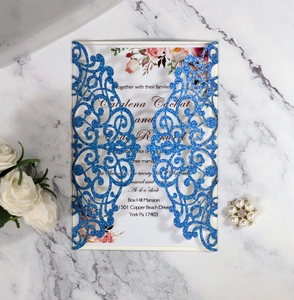 Detail of blue glitter laser-cut wedding invitation with elegant floral insert and envelopes