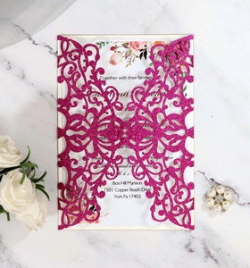 Detailed laser-cut glitter pink wedding invitation with floral insert on marble background