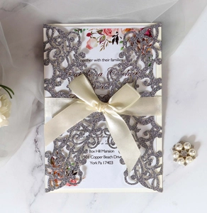Detail of silver glitter laser cut wedding invitation with beige ribbon on marble background