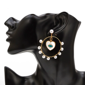 Detailed shot of large golden hoop earring with white pearls and blue evil eye heart charm