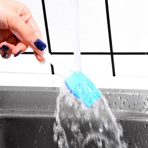 Blue heat-resistant silicone basting brush being rinsed under a kitchen faucet