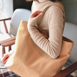 Large beige canvas tote bag with brown leather straps shown in a lifestyle setting