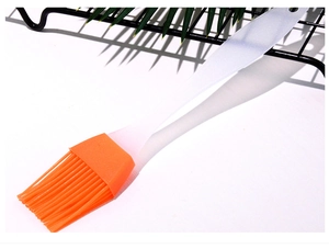 Detail of an orange silicone brush head with a white handle for baking and BBQ
