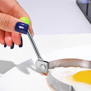 Thickened stainless steel fried egg mold with green handle used in a pan for round eggs