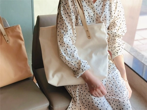 Detail of canvas tote bags with leather handles in cream and brown on a wooden bench