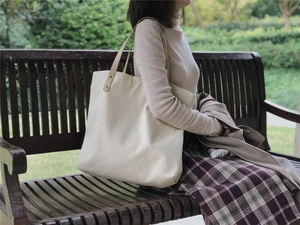 Detailed shot of heavy canvas tote with brown faux leather straps on a park bench