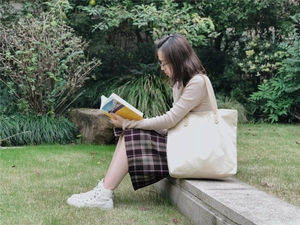 Close-up of a large cream canvas tote bag with brown PU leather handles in a park setting