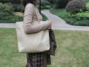 Close-up of large canvas tote bag with leather straps and rivet details outdoors