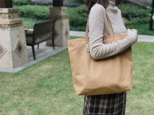 Detail of canvas tote bag with leather handles and metal rivets on model in park