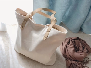 Detail of cream canvas tote bag with brown faux leather handles and metal rivet reinforcement