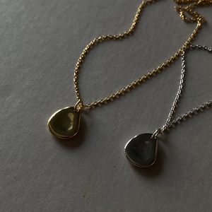 Detailed view of silver and gold teardrop pendants on fine chains over grey surface
