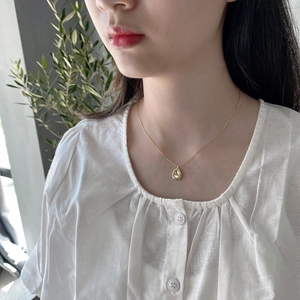 Close-up of a minimalist golden teardrop pendant necklace worn on a female model