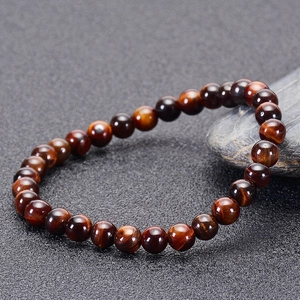 Macro shot of 10mm red tiger eye beads bracelet with silk luster on pebble stone