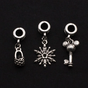 Macro shot of silver charms in shoe, snowflake, and Mickey-head key designs on black background