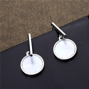 Minimalist silver geometric earrings with white round shell pendants on a black display base