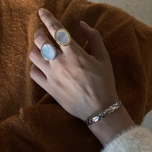 Detail of 925 sterling silver shell rings and textured bangle on model in warm lighting