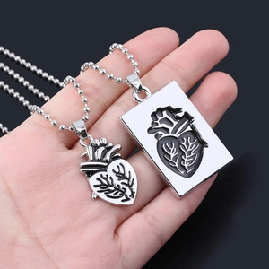 Detail of silver couple heart pendant necklaces with bead chains held by a hand