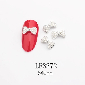 Détail macro de breloque nœud argentée avec perles sur un ongle rouge artificiel