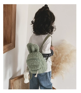 Vue arrière d'un sac à dos lapin en peluche vert clair porté par un enfant à la maison