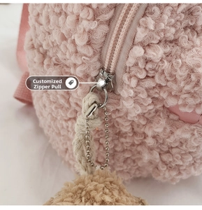 Détail de la texture peluche rose avec fermeture éclair argentée et pompon marron
