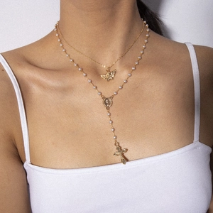 Double-layered gold necklace with angel pendant, pearls, and a cross tassel on a model