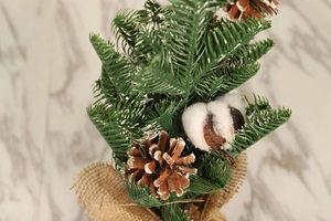 Close-up of mini PE Christmas tree with linen base, pine cones, and snowy details