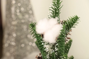 Close-up of frosted Christmas tree branch with pine cones and cotton on snowy background