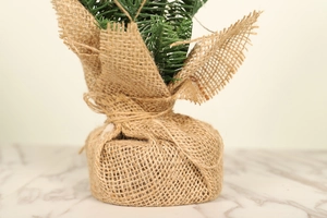Close-up of mini Christmas tree base wrapped in brown burlap with a rustic twine bow tie