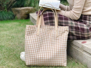 Foto lifestyle di una grande borsa tote a quadri con manici in pelle marrone su gradini di pietra