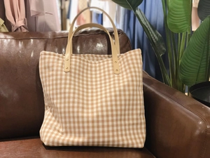 Dettaglio della borsa tote a quadretti beige con manici in pelle su divano marrone