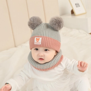 Detail of warm grey and pink knit baby hat with two pom-poms and matching neck warmer