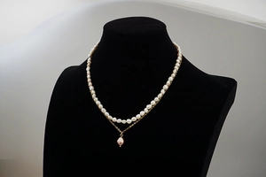 Détail d'un collier double rang en perles baroques et chaîne dorée sur buste en velours noir
