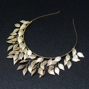 Macro detail of golden metal headband featuring finely carved leaves on textured black background