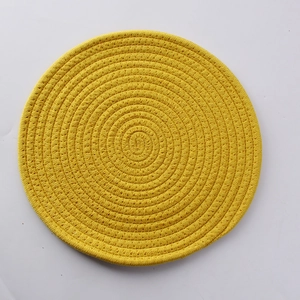 Top view of a yellow woven cotton coaster showing detailed spiral texture and heat resistance