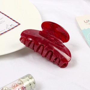 Detail view of a marble red acetate hair claw clip on a minimalist white background