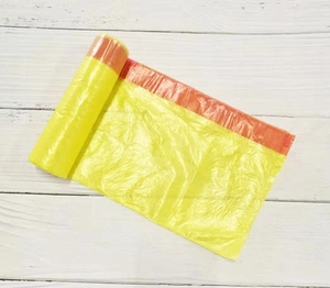 Detail of yellow drawstring trash bag roll with orange pull handles on white wood background