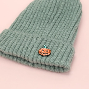 Close-up of orange pumpkin embroidery on a green ribbed knit beanie for Halloween