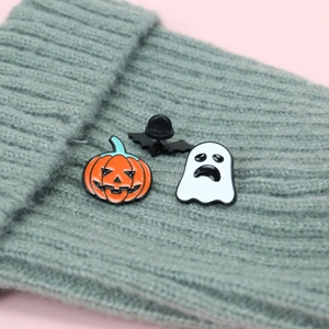 Detailed close-up of Halloween ghost and pumpkin enamel pins on a gray knitted beanie hat