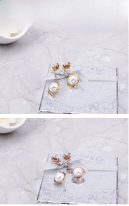 Détail de boucles d'oreilles lune et perle sur un coffret argenté et fond marbre