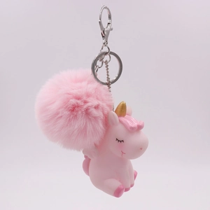 Pink unicorn keychain with fluffy pom pom and golden horn on white background