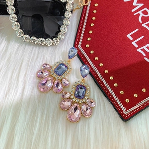 Close-up of purple and pink teardrop earrings with crystals on a white plush rug
