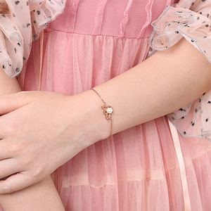 Roségoldenes Perlenarmband am Handgelenk mit elegantem rosa Spitzenkleid im Hintergrund