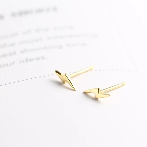 Macro shot of minimalist gold lightning bolt stud earrings with polished finish detail